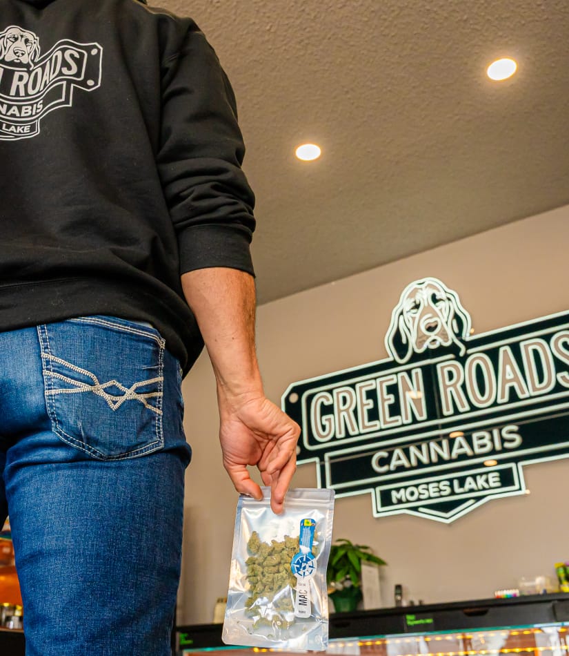 quality-and-education customer holding package of cannabis flower for purchase with green roads neon sign in background